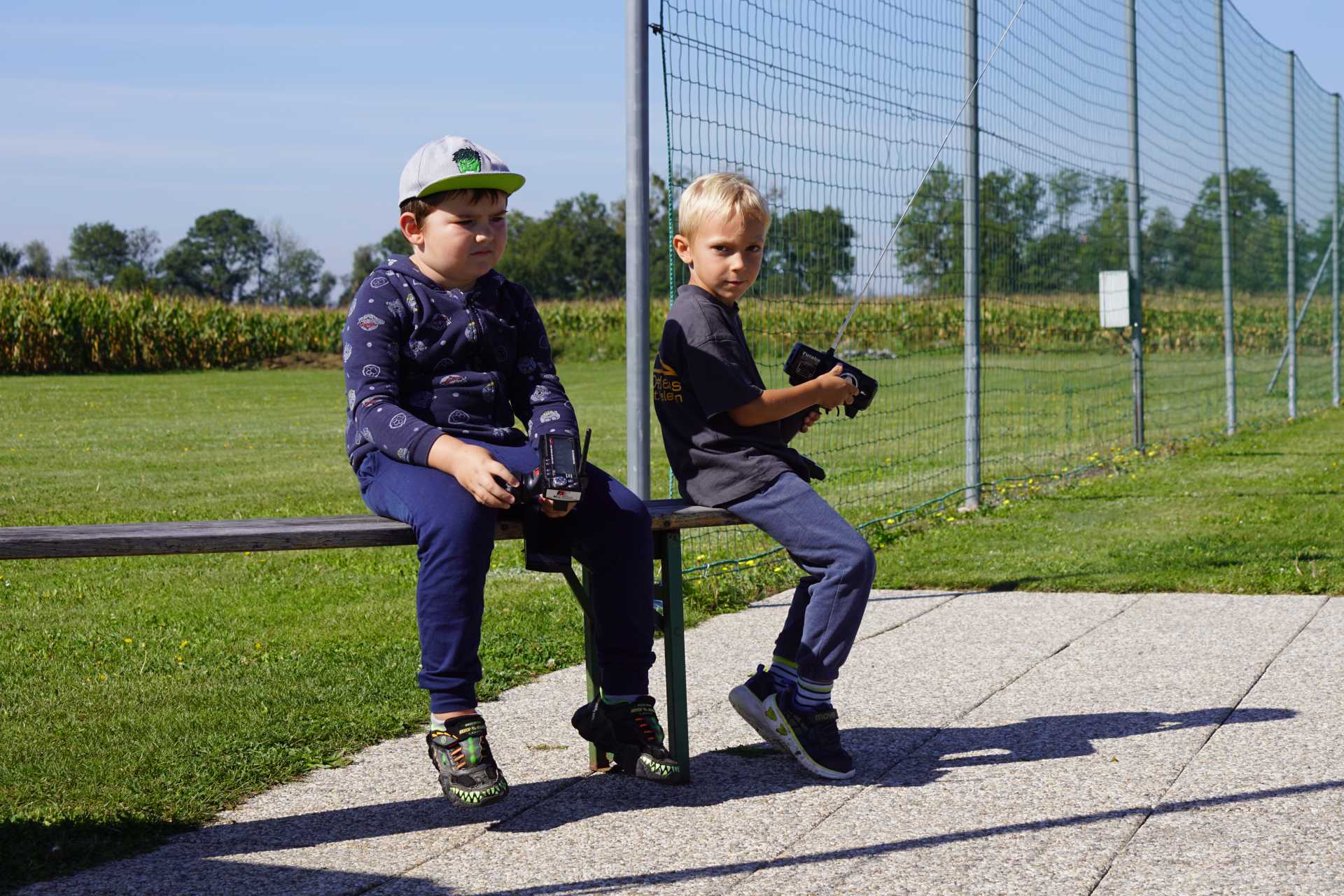 Kinder Freunde sitzen auf der Bank und steuern gemeinsam ihre RC-Cars